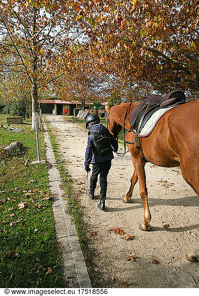 Young boy walking with horse to the stable after riding.