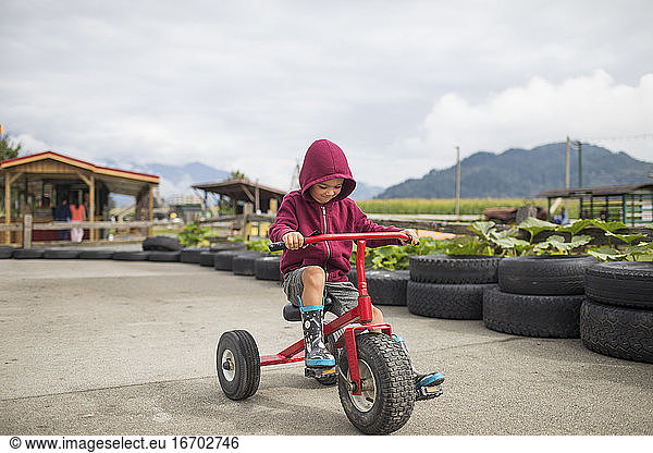 Young boy wearing hoody pedals oversized tricycle on racetrack.
