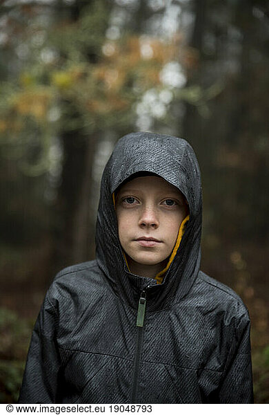 Young boy wearing raincoat with hood looking at camera
