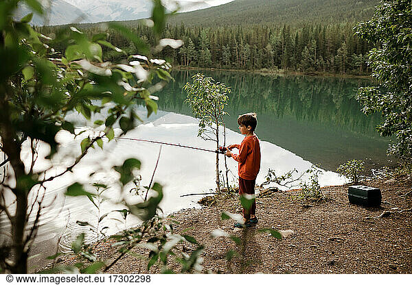 Young boy wearing red fishing in a green lake in the morning