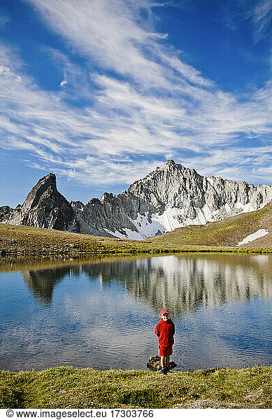Young boy wearing red  standing in front of alpine lake  scenic peaks