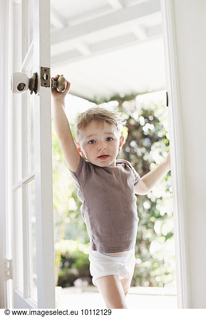 Young boy wearing T-Shirt and pants opening a door.