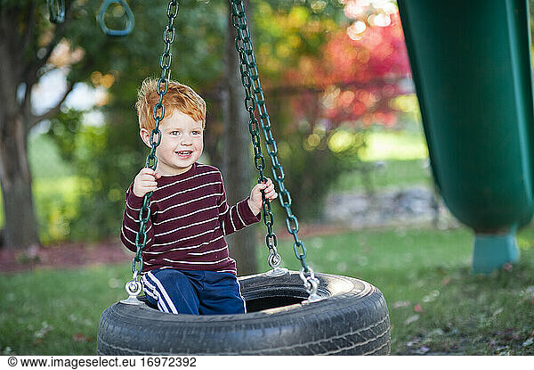 Young boy 3-4 years old laughing and swinging on tire swing outdoors