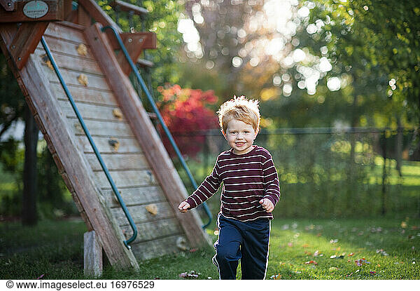Young boy 3-4 years old running through grass in backyard during fall