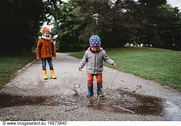 Young boys jumping in the puddles at the park on cloudy day