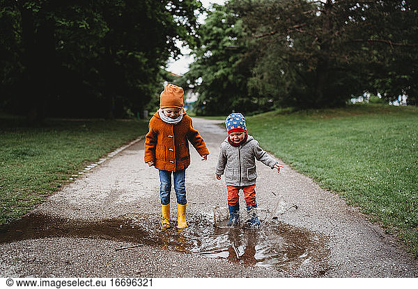 Young boys jumping in the puddles at the park on cloudy day