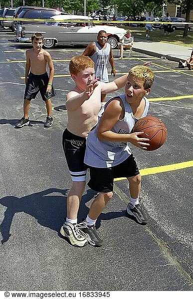 Young Boys male participants play 3 on 3 basketball outdoors.
