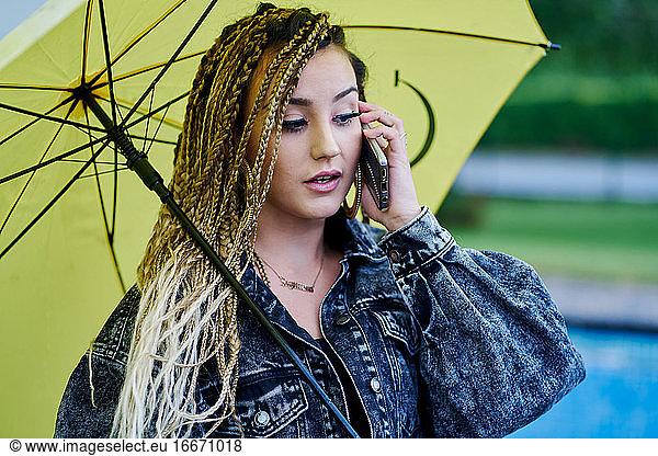 Young braided hair woman talking on smartphone and holding an umbrella. Fashion concept