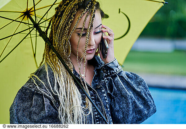 Young braided hair woman talking on smartphone and holding an umbrella. Fashion concept