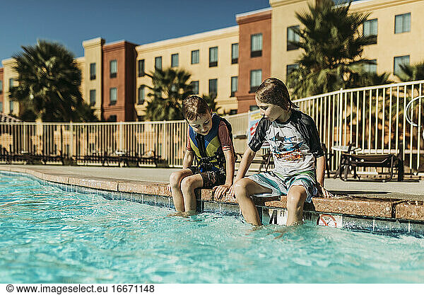 Young brothers sitting next to each other poolside on vacation