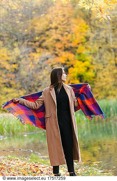 Young brunette girl enjoying walking in park wrapped in plaid
