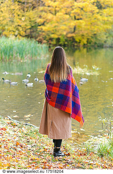 Young brunette girl walking by the lake wrapped in plaid