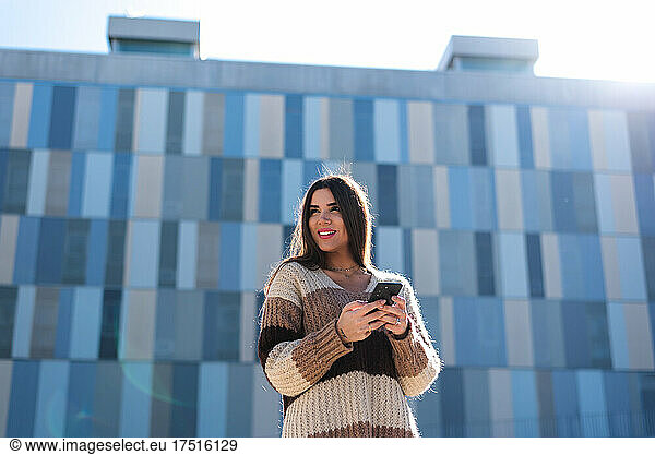 Young brunette woman smiling and using her mobile phone in the city.