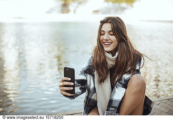 Young brunette woman using smartphone and taking a selfie at lake