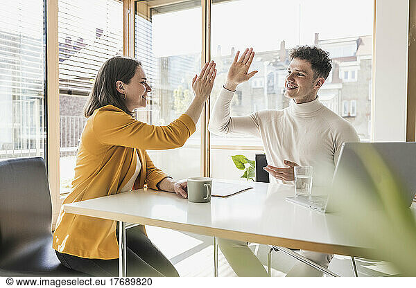 Young businessman and businesswoman high fiving in office