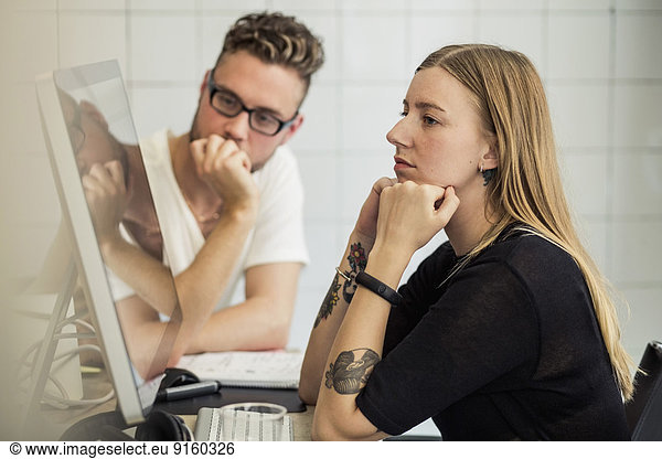 Young businessman and businesswoman looking at computer monitor in creative office