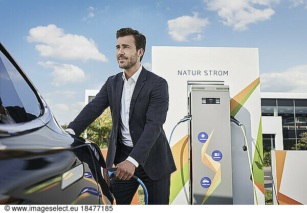 Young businessman charging car at electric vehicle station