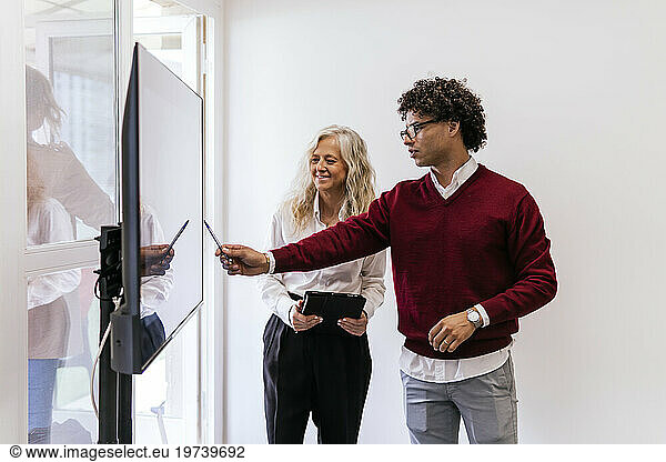 Young businessman explaining to colleague through presentation on screen at work place