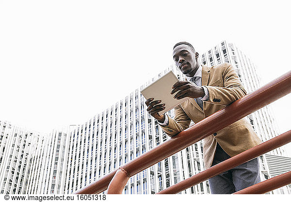 Young businessman leaning on a railing in the city using a tablet