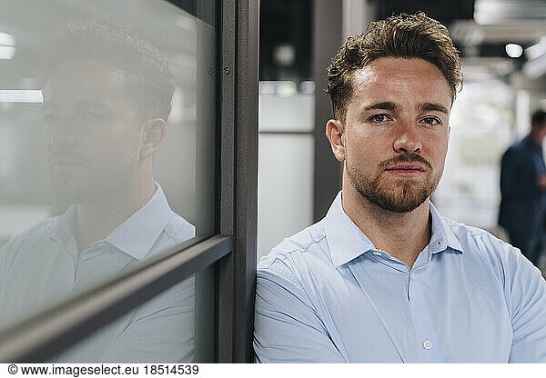 Young businessman leaning on wall in office