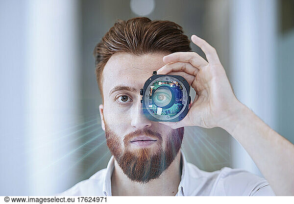 Young businessman looking through open camera lens at office