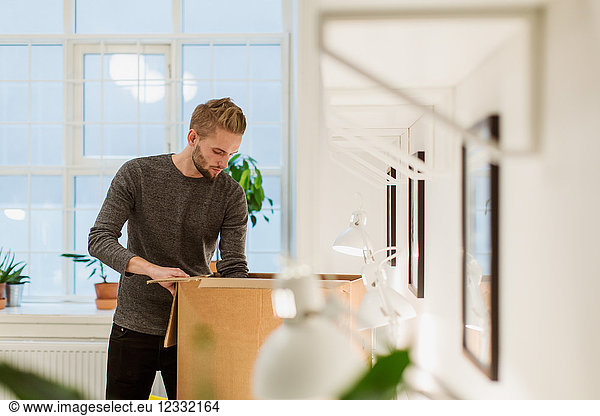Young businessman opening cardboard box at illuminated creative office