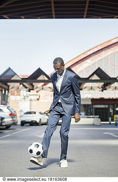 Young businessman playing with soccer ball at parking lot on sunny day