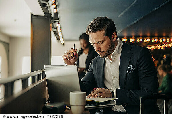 Young businessman reading diary while sitting with laptop in hotel