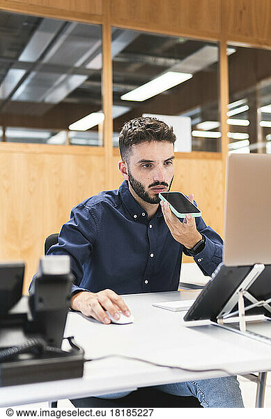 Young businessman talking on smart phone and using laptop at desk