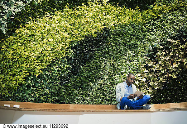 Young businessman using digital tablet in front of green plant wall