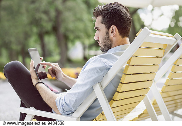 Young businessman using digital tablet on lounge chair at park
