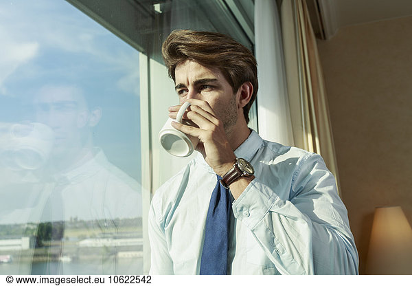 Young businessman with mug looking through window