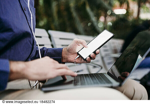 Young businessman with smart phone using laptop