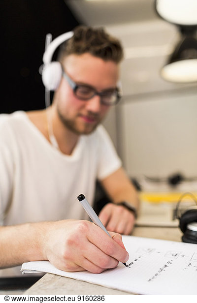Young businessman writing on book in creative office