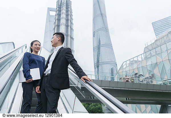 Young businesswoman and man talking while moving up city escalator  Shanghai  China