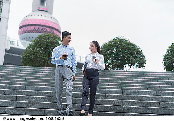 Young businesswoman and man with takeaway coffee moving down city stairway  Shanghai  China