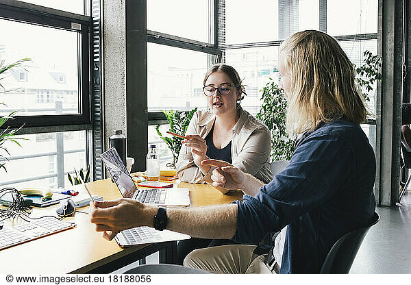 Young businesswoman discussing over laptop with colleague at desk in startup company