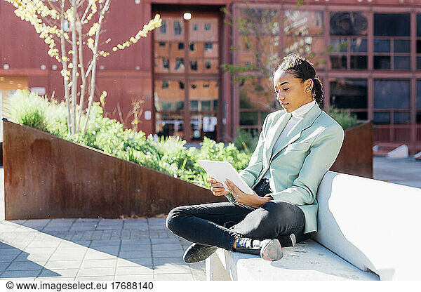 Young businesswoman freelancing over tablet PC sitting on bench