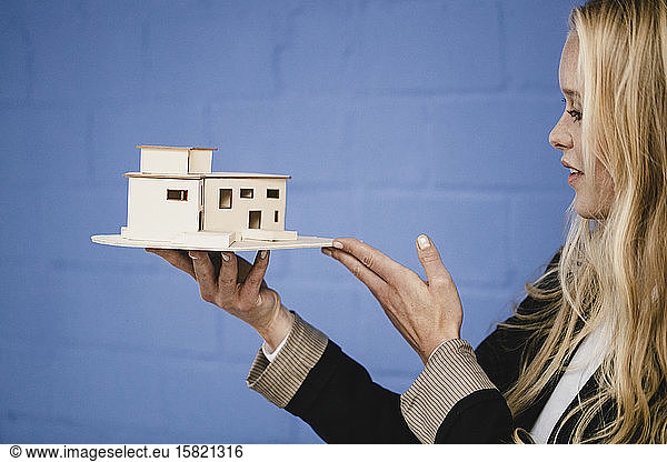 Young businesswoman holding architectural model at blue wall