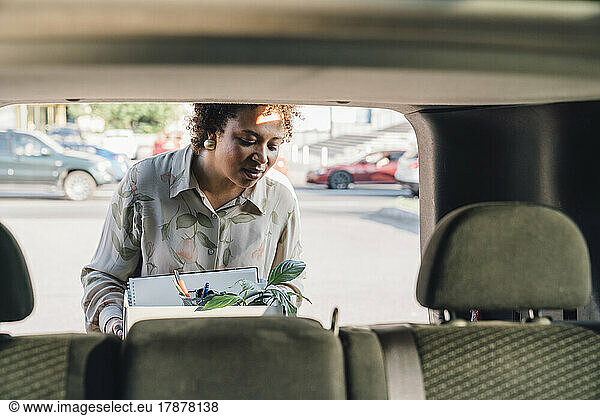 Young businesswoman keeping box in car trunk