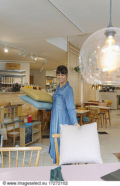 Young businesswoman keeping pillow on chair in cafe