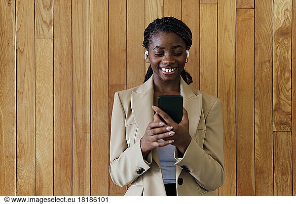 Young businesswoman looking at mobile phone in front of wooden wall