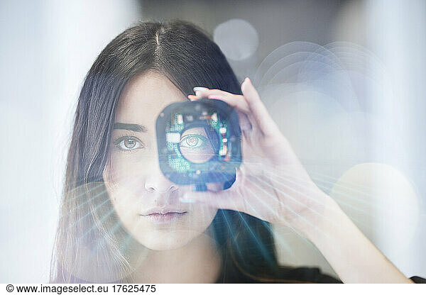 Young businesswoman looking through open camera lens at office