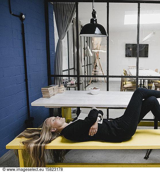 Young businesswoman lying on a bench in a loft office with closed eyes