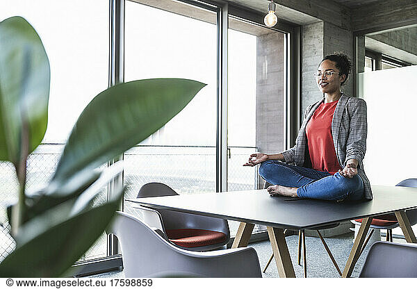 Young businesswoman meditating on desk in office