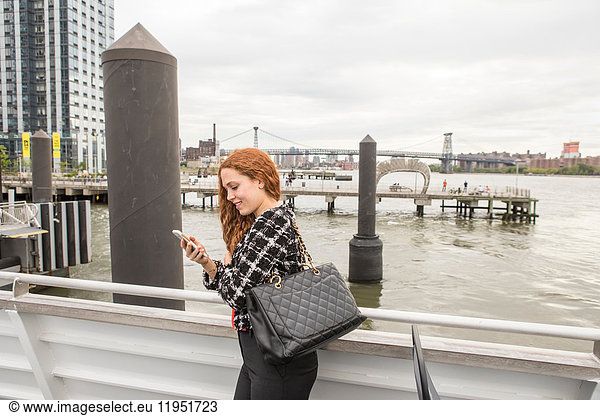 Young businesswoman on ferry deck looking at smartphone  New York  USA