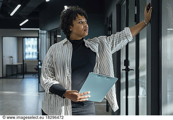 Young businesswoman standing with clipboard in office