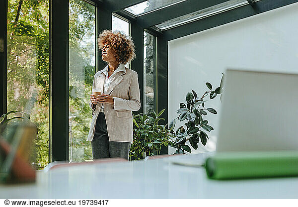 Young businesswoman standing with eyes closed near window in office