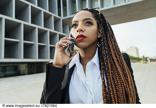 Young businesswoman talking on smart phone outside office building