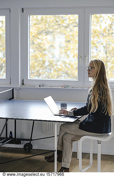 Young businesswoman using laptop on table tennis table in office